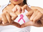 Woman in white tank top making a heart with her hands and holding pink ribbon for breast cancer awareness 
