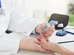 Finger on female hand getting pricked with blood sugar meter for diabetes testing by healthcare professional in white coat
