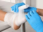 Two hands in blue medical gloves wrapping patients foot and ankle with gauze bandage for pressure injury or ulcer