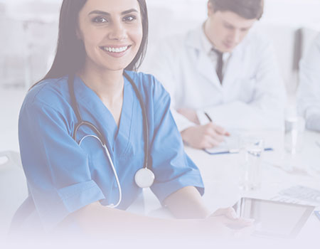 Female nurse in blue scrubs with stethoscope around neck sitting in front of male doctor in white coat