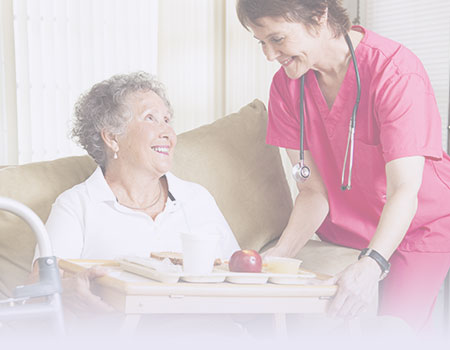 Nurse in pink scrubs serving food on a tray to elderly woman on couch representing home health nursing CEUs