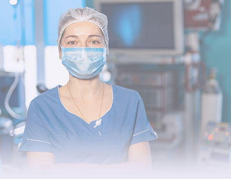 Female nurse in scrubs, mask and hair net standing in operating room representing perioperative nursing CEU