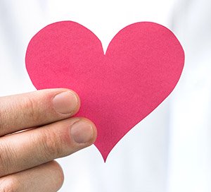A hand holding up a paper cut out of a heart