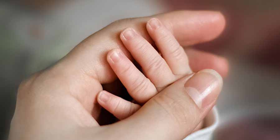 Adult hand grasping gently a baby hand