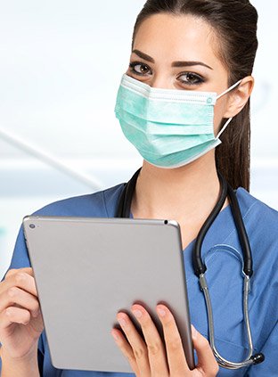 Nurse wearing a protective mask works intently on her tablet.