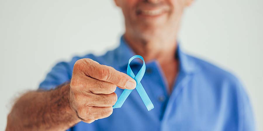 Man in blue shirt holding up a blue ribbon representing Prostate Cancer support.