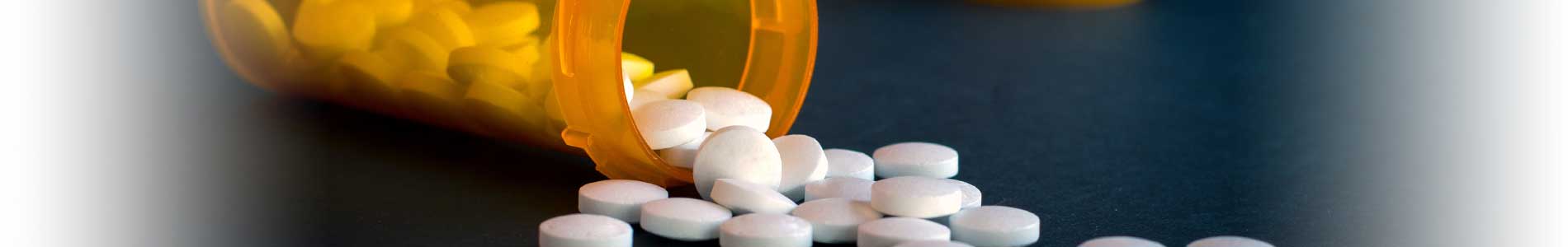 Three orange pill bottles with white lids and prescription stickers and one pill bottle with white round pills falling out  