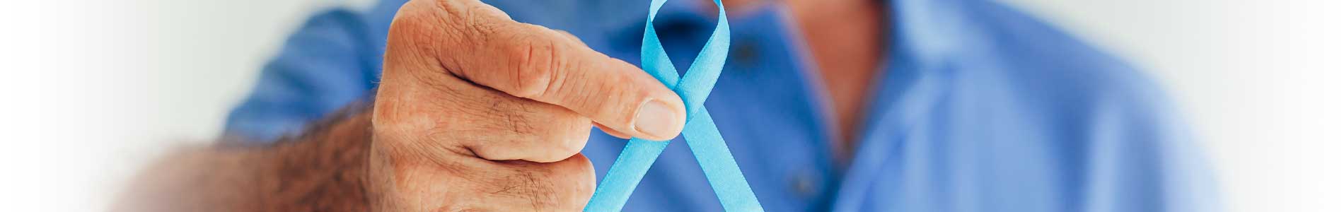 Torso of older male nurse in blue scrubs holding blue ribbon for prostate cancer awareness in his right hand