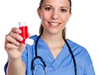 Smiling female nurse in blue scrubs with black stetoscope around her neck holding a red and white Asthma inhaler in her hand