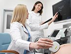 Blond female doctor sitting in blue chair performing ultrasound on pregnant patient while nurse watches monitor