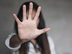 Woman with long dark hair in white shirt with raised hand covering her face to prevent herself from sexual harassment