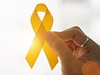 Right female hand with gold ring on index finger holding yellow ribbon for suicide prevention into the sun