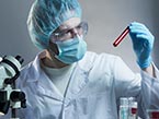 Medical professional with lab coat, face mask, gloves and hair net, holding and looking at blood testing tube for pathogens