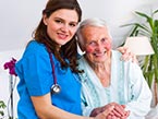 Young female nurse in blue scrubs with black stethoscope hugging and caring for elderly woman with short gray hair