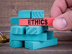 Right hand pulling red wooden block with the word Ethics written on it out of stack of blue wooden blocks