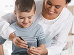 Woman in white shirt hugging young boy from the back and pricking his finger for childhood diabetes testing