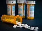 Three orange pill bottles with white lids and prescription stickers and one pill bottle with white round pills falling out  