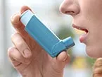 Woman's face from the side holding a blue COPD inhaler with her right hand towards her mouth