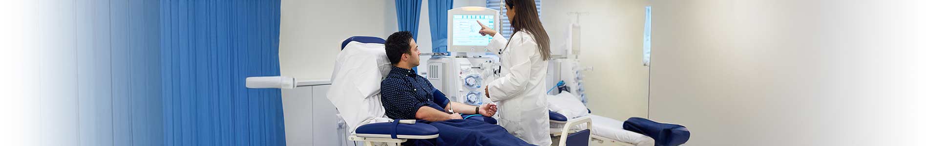 Male patient receiving treatment from a dialysis machine and listening to a nurse discussing his chronic kidney disease.