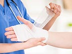Nurse in blue scrubs and stethoscope taking care of wound on right arm of a patient by bandaging with gauze