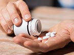 One hand holding a white prescription bottle, the other hand open with a few white pills in it.