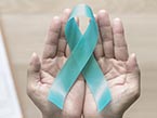Two hands holding up a teal colored ribbon, the symbol of sexual violence prevention, with a background of a doctors notepad and stethoscope