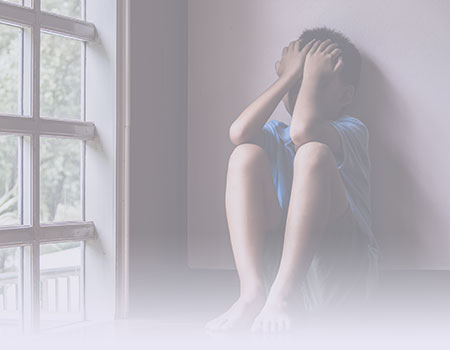 Young boy sitting on floor holding his face in his hands to represent abuse, neglect and violence