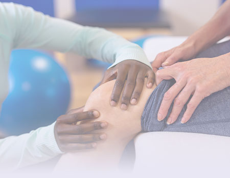 Hands of black healthcare provider touching patients knee and blue ball in back representing rehabilitation nursing CEUs